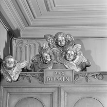 Katolska kyrkan. Änglaskulpturer ovanför biktstolarna. Text: Pax Domini