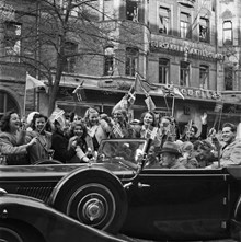 Fredsdagen den 7:e maj 1945. 

Glada människor i bilar och på gatan viftar med flaggor på Birger Jarlsgatan.