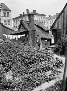 En man och två barn står på gårdssidan av Bengt Ekehjelmsgatan 16. Husen i fonden ligger vid Högbergsgatan 72-70. Den här delen av Bengt Ekehjelmsgatan är nu igenlagd och ingår i kv. Hållkarlen
