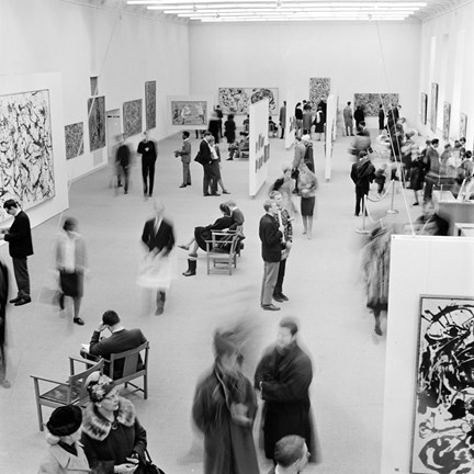 En bild fotograferad uppifrån över en av utställningshallarna på Moderna museet. Väggarna är vita och ett tjugotal upphängda målningar syns på bilden, med besökare som vimlar runt i hela rummet.