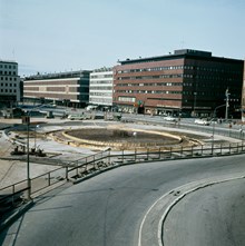 Vy från Malmskillnadsgatan mot varuhusen Åhlens och EPA. Fontänen vid Sergels Torg under uppbyggnad med armeringsjärn och gjutformar