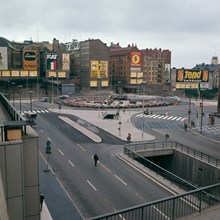 Från gångbron i Stockholmsterrassens norra del mot Sergels Torgsrondellen. Fasadreklam i kv. Skansen och Fyrmörsaren. Fontänen under byggnad