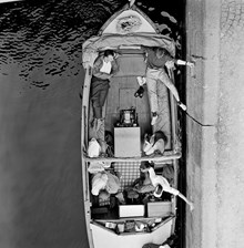 Passagerare i motorbåt med upprullat kapell väntar på slussning