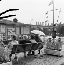 Strömgatan. Fem kvinnor sitter på en parkbänk vid ett sightseeingkontor