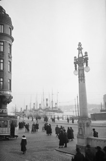 Feiths hörn fotograferat från Dramaten med Strandvägen och Nybroviken i fonden. Människor på gatan.