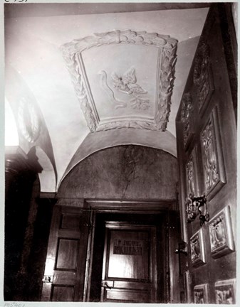 Detalj av ett trapphus. till höger en snidad trädörr, rakt fram en dörr med skylten AB Asklunds bokbinderi. i taket utsmyckning med en fyrkantig krans av kärvar.