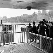 Färjan ""Djurgården 2"" på väg att lägga till invid Räntmästartrappan. Passagerare väntar i kö. I bakgrunden Stadsgårdshamnen