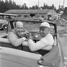 Grupporträtt av Lennart Hyland och Gunnar Olsson i en sportbil. I bakgrunden en Esso-mack