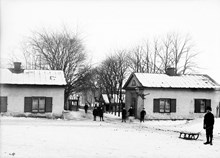 Några barn står vid Ladugårdslandstull mellan tullhusen. Tullhusen låg vid nuvarande Karlaplan, de revs 1896
