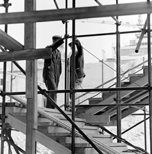 Två byggnadsarbetare i en byggnadsställning med trappor