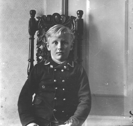 Hans Strindberg sju år gammal, klädd i en mörk dubbelknäppt jacka, sitter på en utsirad stol. Fotograferad av pappa August Strindberg