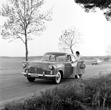 Ford Zephyr parkerad vid kanten på en landsväg. En kvinna står och samtalar med föraren