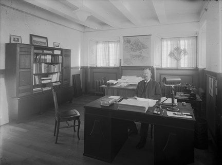 arkitekt Per Hallman sitter i sitt arbetsrum bakom ett skrivbord. 
