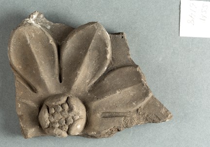 Fragment av lergods. På fragmentet syns delar av ett ornament i form av en stiliserad blomma. 