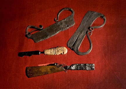 Två medeltida eldstål och två små knivar med trähandtag. Fotograferat mot rödbakgrund.