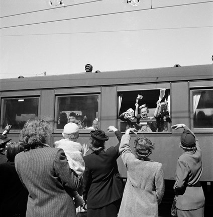 I fönstren till en järnvägsvagn står barn och vinkar. På perrongen står kvinnor, förmodligen barnens mödrar, och tar adjö.
