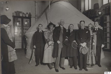 Män i kostym framför en jurta i ett utställningsrum. I bakgrunden syns montrar med föremål.