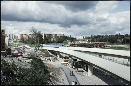 Vy över Kista med bro och tunnelbanetåg, gångvägar och flerfamiljshus.