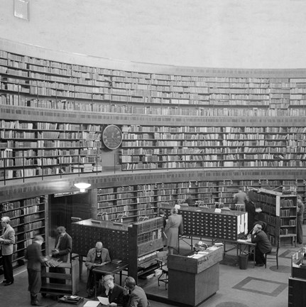 Stadsbibliotekets rotunda med bokhyllor, katalogskåp, informationsdisk och besökare.