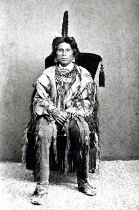 Svartvitt fotografi av en ung man i indiansk scenkostym och med fjäder i håret.