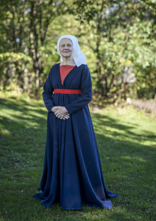 Foto av en kvinna klädd i återskapad dräkt som står med ansiktet mot kameran med träd i bakgrunden 