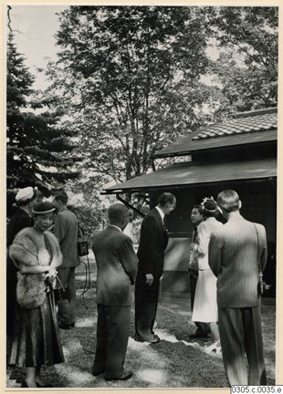 Män i kostym och elegant klädda kvinnor, utomhus vid det japanska tehuset.