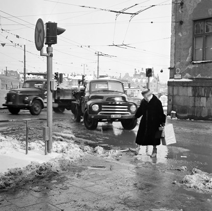 En äldre kvinna korsar gatan, med pölar av smält snö.