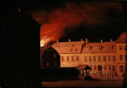 En brand har brutit ut i ett hus. Lågorna färgar himlen röd och lyser upp fasaden på den långa tvåvåniga byggnaden.
