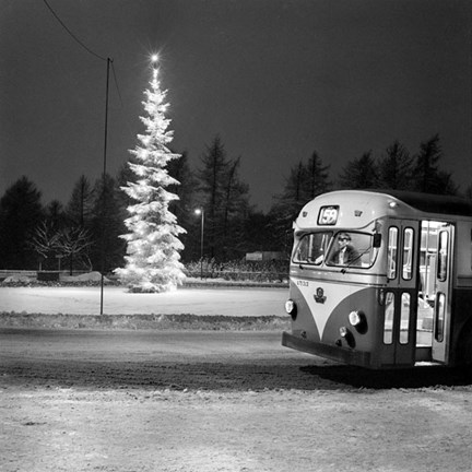 En upplyst buss står parkerad. I bakgrunden syns en upplyst julgran. Det ligger snö på marken och det är mörkt ute.