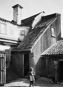 Ett barn står på gårdssidan av Västra Kvarngränd 6 och 8. Nuv. kv. Kvadraten ung. norr om Allhelgonagatan, tidigare Gotlandsgatan