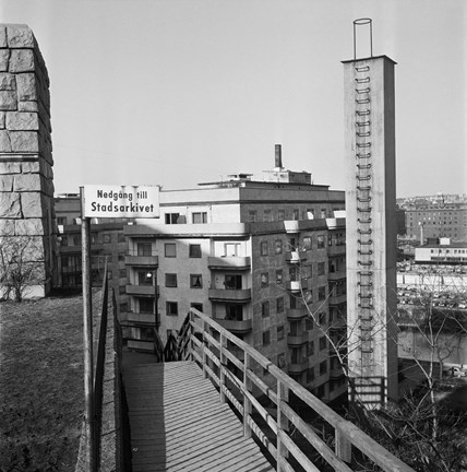 Ett torn i sten och en skorsten, första delen av uppförandet av Stadsarkivet. En skylt med texten Nedgång till Stadsarkivet. Flerbostadshus i bakgrunden.