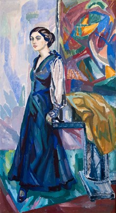 Carin Östberg bärandes en lång blå klänning. Hon står lutandes mot ett bord med en färgglad bakgrund.