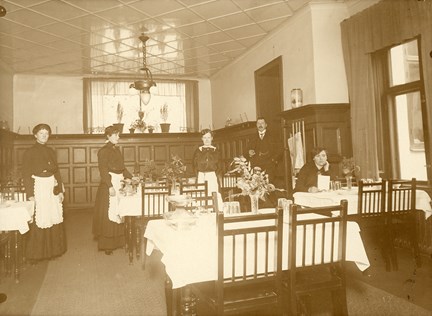 Bruntonad interiörbild av andraklassmatsal i restaurang Pilen, med personal i bakgrunden