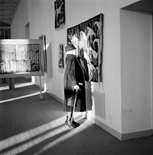 Äldre dam med käpp betraktar på nära håll ett textilt verk på utställning i Moderna museet