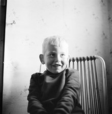 Porträtt av liten pojke, Thomas Risberg, i stol mot bakgrund av blommig tapet. Rävsnäs.