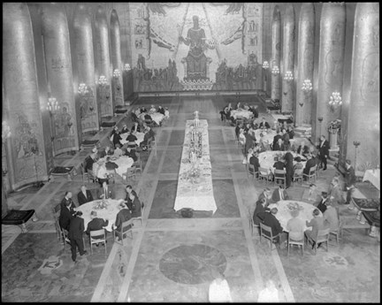 Åtta runda bord med sittande gäster och i mitten av salen ett långsmalt, festligt dukat bord.