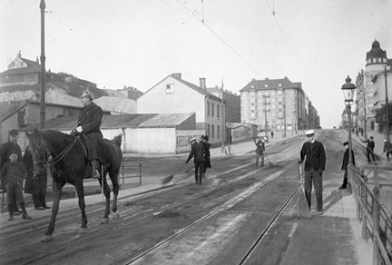 Studenter i vita mössor är strejkbrytare och sopar gatan under renhållningsstrejken 1905. De skyddas av poliser på hästar.