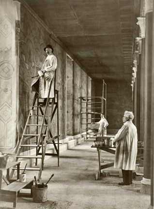 Svartvitt fotografi ifrån arbetet med muralmålningen Staden vid vattnet i Prinsens galleri i Stockholms stadshus. I bilden syns tre män, bland annat prins Eugen ståendes på en stege, alla har vita målarrockar på sig. 