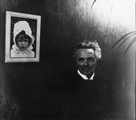 August Strindberg i sitt hem på Drottninggatan 85, bredvid ett inramat fotografi av yngsta dottern Anne-Marie.