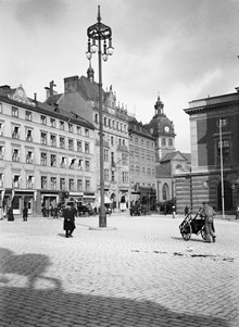 Gustav Adolfs Torg mot Arsenalsgatan med Jakobs kyrka i fonden. En man med dragkärra passerar torget. Operan stod klar 1898