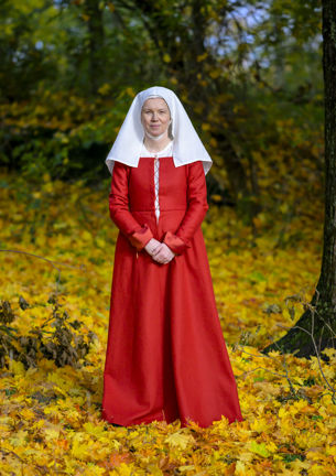 Foto av en kvinna klädd i återskapad dräkt som står utomhus bland träd och löv.