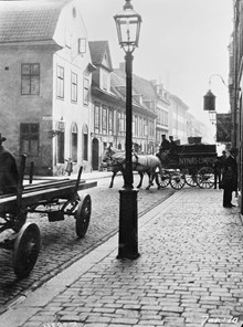Regeringsgatan 54 A, B och C söderut från hörnet av Lästmakargatan. Ett hästfordon, två hästar och en vagn med texten Nynäs Limpor, passerar gatukorsningen