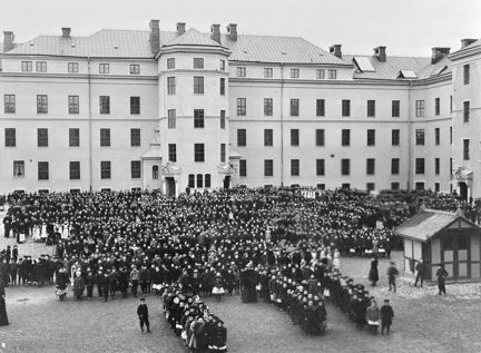 Svartvitt foto med hundratals elever i rader utanför en skolbyggnad.