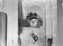 Porträtt av en okänd man i skärmmössa från Stockholms Spårvägar, förmodligen en konduktör, som tittar ut igenom en spårvagns isiga fönster