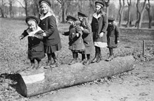 Barn leker i en park på en kullfallen trädstam.