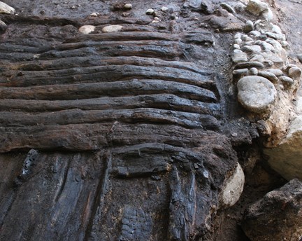 Fotografi som visar brädor som ligger vertikalt  på en rustbädd i sten. 
