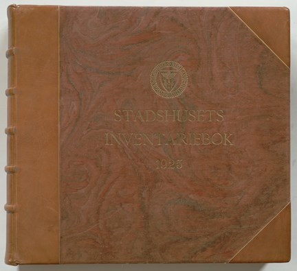 Framsida till den tjocka boken, som är inbunden med marmorerad och har rygg och hörn i läder. Titel "Stadshusets inventariebok 1925"