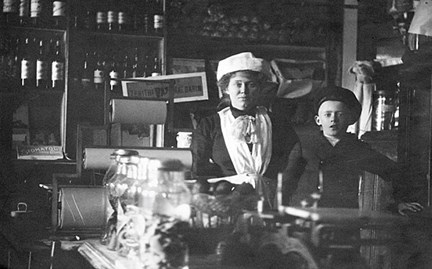 Interiör från Livsmedelsaffär på Götgatan 77 omkring år 1915. På bilden syns fru Augusta Norgren tillsamman med sonen Harry.