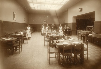 Interiörbild av tredjeklassmatsal i restaurang Pilen, med personal i bakgrunden och dukade bord i förgrunden