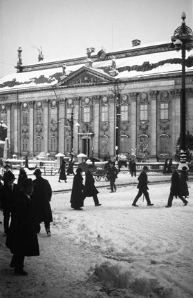 Snön ligger vit och människor promenerar kors och tvärs över en öppen plats framför ett 1600-talspalats.
